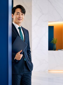 Vertical portrait of businessman holding a folder in a modern office. Professional in navy suit with copy space