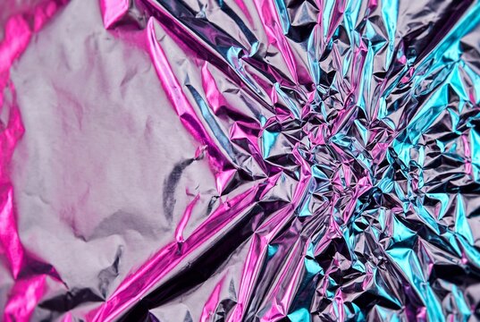 Abstract crumpled metallic foil texture with vibrant pink and blue neon light reflections, featuring a smooth silver copy space area on the left side