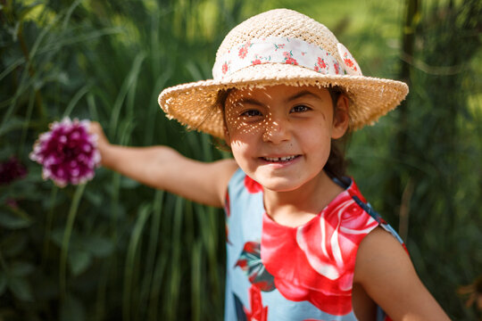 Cute Little Girl in Floral Dress Playing with Purple Flower Outdoors