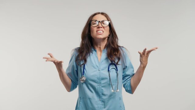 Angry Female Doctor in Blue Medical Coat Shouting Directly at Camera, Expressing Rage, Frustration and Emotional Stress in Studio