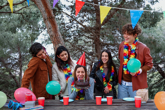 Hispanic group of friends celebrating a birthday party outdoors. Diverse people multi age and multicultural eating cake and holding gifts