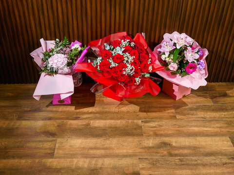 Three premium flowers bouquets are standing on a wooden floor by a dark brown wall. Special event decorations and present concept. Pure beauty and craft. Fancy artistic design.