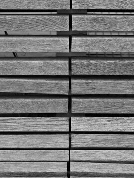 black and white diagonal view shows the parallel wooden slats of a bench or boardwalk surface with visible grain textures