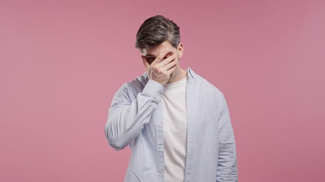 Embarrassed Man Facepalming in Secondhand Embarrassment After Witnessing an Awkward, Cringeworthy Situation on Pink Studio Background