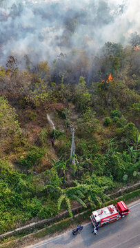 Aerial view of a forest fire being extinguished by a firefighter with a hose, with a fire truck parked on the nearby road in Kotabaru, Kalimantan Selatan, Indonesia.