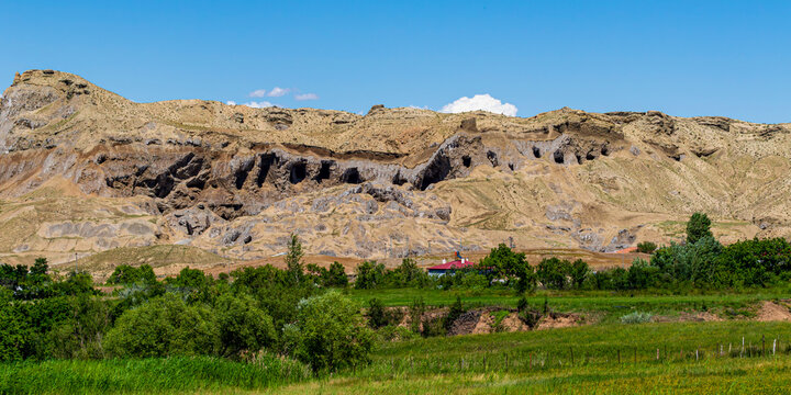 Wide panoramic view of ancient rock-cut cave dwellings and tombs carved into a cliff above green valley