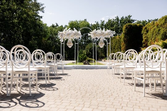 Outdoor wedding ceremony site with white arch and chiavari ghost chairs