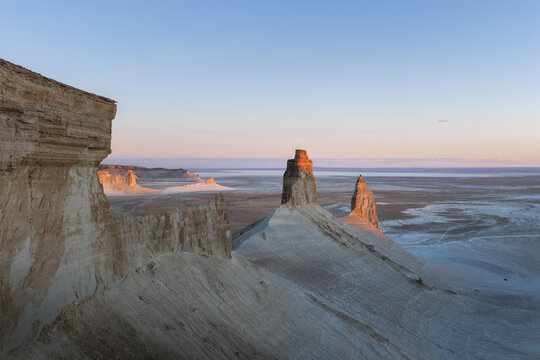 Aerial view of the Lower Fangs rock formations in the Bozhira tract, featuring dramatic limestone cliffs, desert landscape, and soft sunset light in Karakiya District, Mangystau, Kazakhstan.