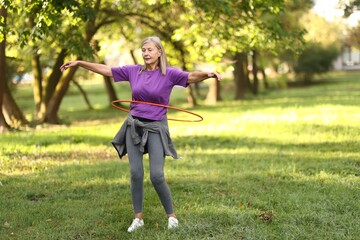 Senior woman exercising with hula hoop outdoors, space for text © New Africa