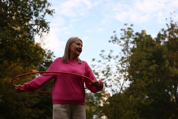 Senior woman exercising with hula hoop outdoors, low angle view. Space for text © New Africa