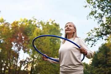 Senior woman exercising with hula hoop outdoors, low angle view. Space for text © New Africa