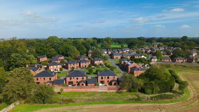 Aerial view of Coton Housing Estate featuring modern red brick houses with dark roofs, manicured lawns, and surrounding greenery in Rugby, England, United Kingdom.