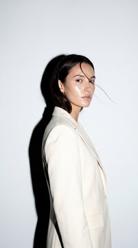 Vertical photo of a young woman in a cream blazer with glossy skin. Fashion portrait with hard shadow and flashburn lighting. Studio beauty shot