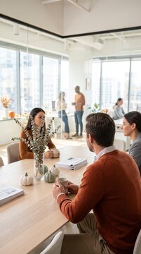 Business team having a meeting at a conference table with autumn halloween decorations. Vertical photo of corporate colleagues discussing work in modern office with city view