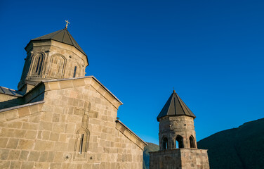 Gergeti Trinity Church with carved stone walls, domed tower and bell tower against a clear blue sky in Stepantsminda, Georgia © Mila