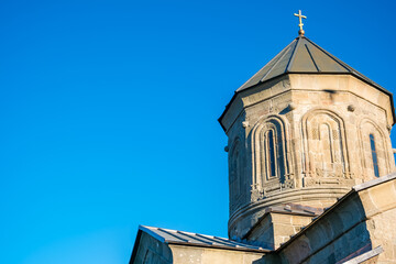 Close view of Gergeti Trinity Church stone tower with carved arches, metal roof and cross against a clear blue sky in Stepantsminda, Georgia © Mila