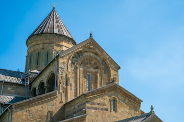 Close view of Svetitskhoveli Cathedral in Mtskheta, Georgia, showing ornate stone carvings, domed roof, crosses, arches, and blue sky © Mila