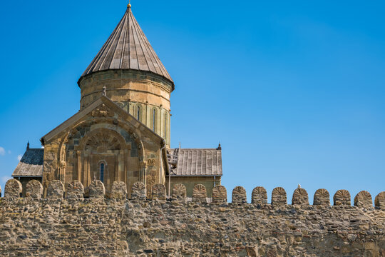 Svetitskhoveli Cathedral in Mtskheta, Georgia, with an ornate stone dome, carved facade, fortified wall, and vivid blue sky