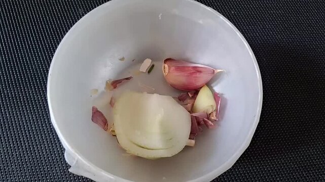 Onion and garlic pieces placed inside a small plastic bowl