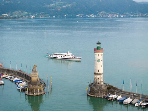 Aerial view of the historic lighthouse and Bavarian Lion statue at the harbor entrance of Lake Constance, with a ferry boat and moored sailboats, Lindau, Bavaria, Germany.