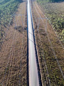 Aerial view of high voltage lines running parallel to a straight dirt road through a forest landscape in Tyrnava, North Ostrobothnia, Finland.
