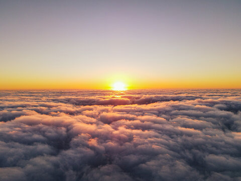 Aerial view of a vibrant sunset glowing above a vast, textured layer of clouds stretching to the horizon in San Diego, California, United States.