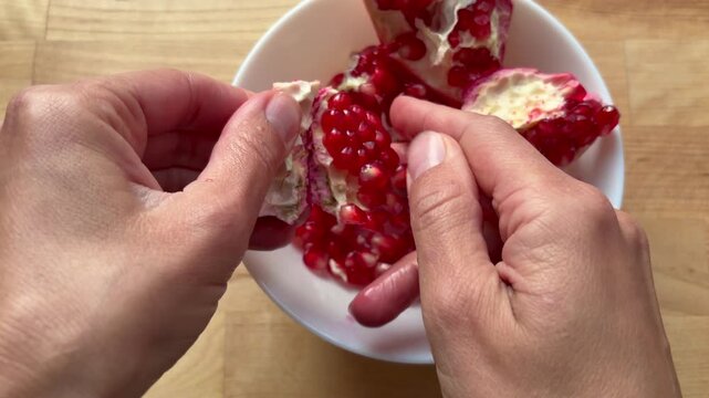 female hands carefully breaking apart a ripe pomegranate over a ceramic bowl. Concepts of fresh fruit, antioxidants and seasonal autumn or winter produce.
