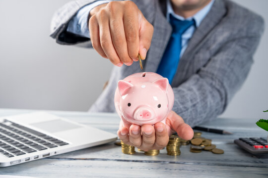 A businessman puts a coin into a piggy bank.