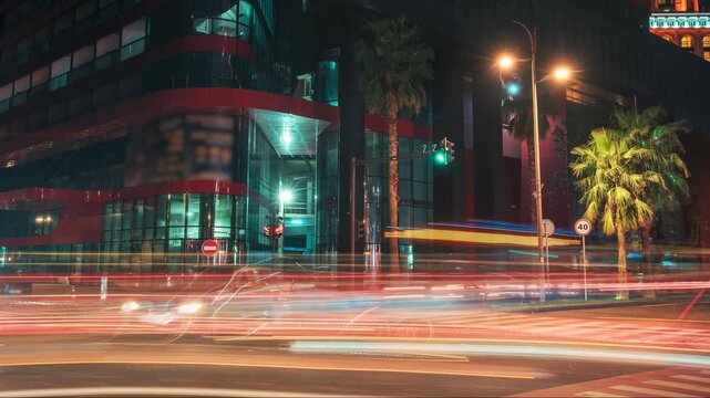 Night City Traffic Timelapse with Long Exposure Car Light Trails at Urban Intersection, Modern Glass Architecture, Illuminated Street and Moving Vehicles After Dark.