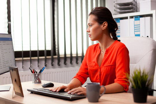 Focus, computer and businesswoman seated in profile at an office desk, typing on a keyboard while reviewing onscreen information, for workplace concentration, professional workflow and digital tasks.