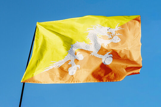 Flag of Bhutan. Flag waving in the wind against a clear blue sky, fluttering on a flagpole outdoors. Bright sunny day, fabric texture, outdoor close-up view
