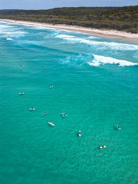 Aerial view of surfers waiting for waves in the turquoise water off the coast of North Stradbroke Island, Redland City, Queensland, Australia.