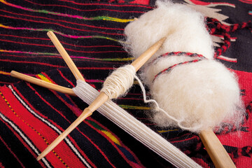 Wooden Spindle with Raw Wool on Striped Red Textile © Jovan Nikolic