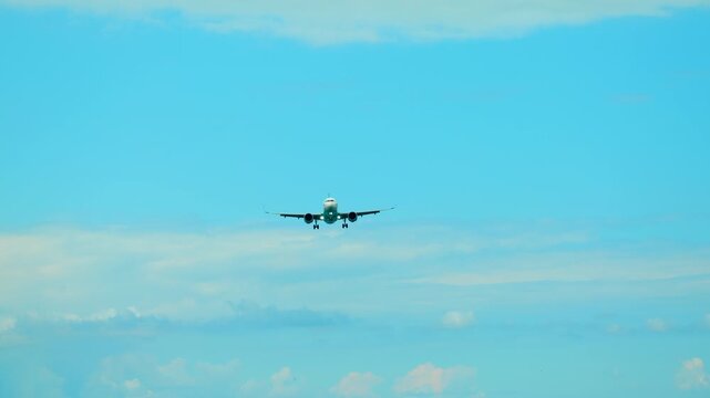 Passenger jet with landing gear down flying on final approach through a clear blue sky with light clouds, getting closer to the runway for a safe touchdown