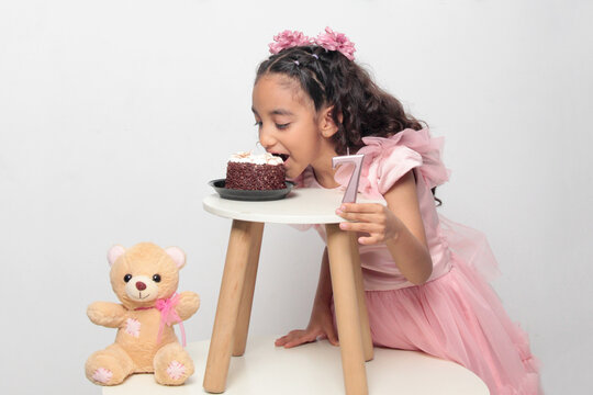 Seven-year-old Latina girl with brown skin and curly hair celebrates her birthday with cake, candle, and colorful decorations
