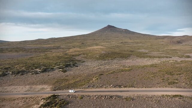 Small white camper van driving along a remote desert highway in front of a large mountain.