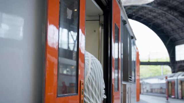 A Caucasian man in a striped shirt turns toward a stopped train and walks along the platform toward its open door.