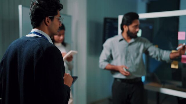 Smiling team leader presenting plan, bearded man explaining project to colleagues in office