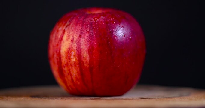 Ripe apple with red stripes on a textured wooden surface, one apple fruit close-up on a dark background