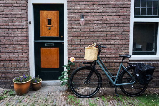 A classic Dutch city bicycle with a wicker front basket and pannier bag parked outside a historic brick house with a green wooden door and potted plants in Haarlem, Netherlands.