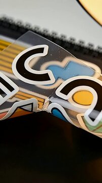 Vertical video: Rotating clear sticker sheet with C decals being held over desk, showing dust, tear