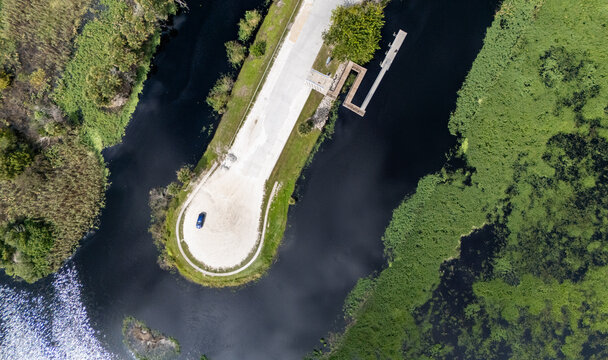 Aerial view of Merritt Island National Wildlife Refuge featuring a boat ramp, a parking area with a parked car, and surrounding marshland and dark water in Oak Hill, Florida, United States.