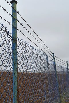 Vertical view of long blue chain link fence with barbed wire extending into distance against overcast sky, security boundary concept