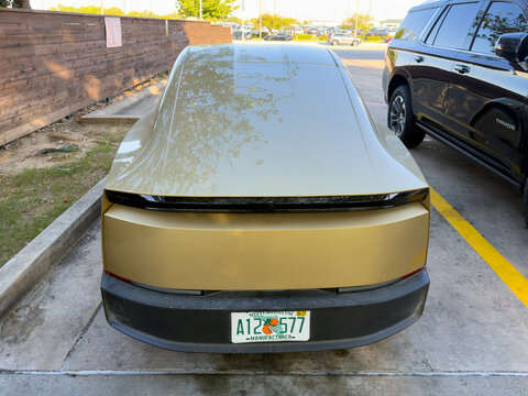 Dallas, Texas, USA - October 15th, 2026: Rear view of gold Tesla Cybercab prototype with Florida license plate parked outside Tesla service center