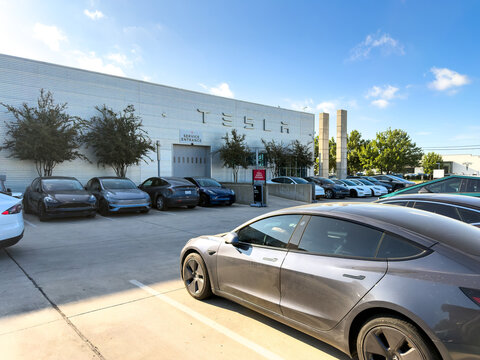 Dallas, Texas, USA - October 15th, 2026: Electric vehicles parked in front of Tesla Service Entrance building under blue sky in sunny weather