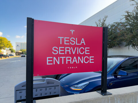 Dallas, Texas, USA - October 15th, 2026: Red Tesla Service Entrance sign standing in parking lot near blue car outside service center facility