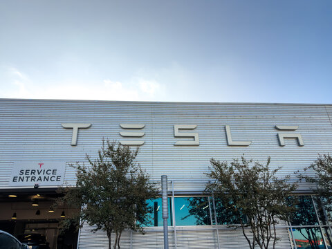Dallas, Texas, USA - October 15th, 2026: Close up of Tesla Service Entrance sign on building facade with trees in front under bright sky