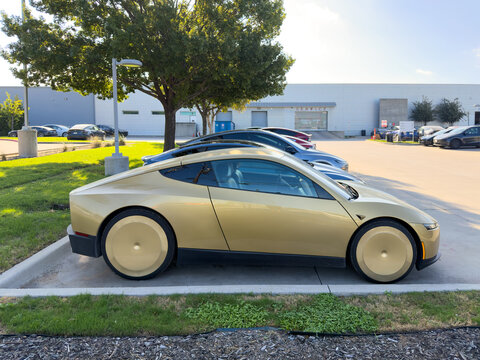 Dallas, Texas, USA - October 15th, 2026: Gold Tesla Cybercab electric vehicle parked on concrete lot outside Tesla service center parking space