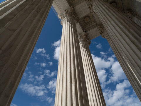 Close-up view of Corinthian marble columns at the U.S. Supreme Court building, with warm light and shadow highlighting the fluted shafts and column bases.