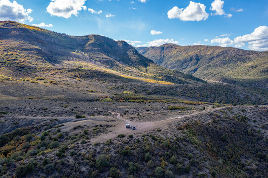 Aerial view of two vehicles in dispersed camping site in Colorado backcountry under sunny autumn cloudscape.